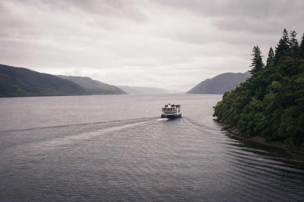 A white cruise boat under way on Loch Ness in soft light, the length of the glen stretching ahead