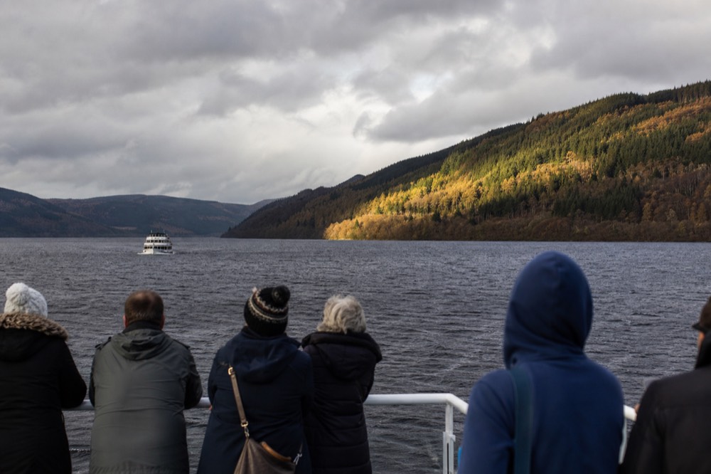 A cruise boat on a misty Loch Ness at dawn with dark hills rising on either side of the glen
