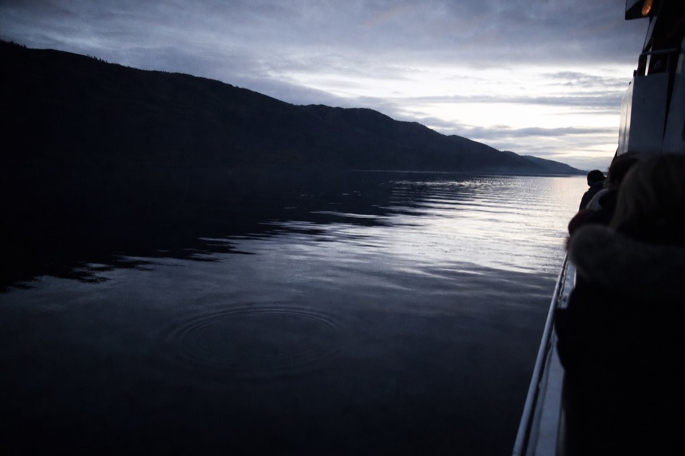 Loch Ness at dusk with a boat silhouetted on dark still water below the ridgeline of the Great Glen